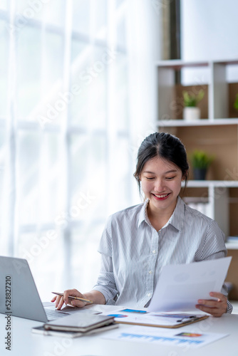 Young woman working on a laptop in the office. Asian businesswoman sitting at her workplace in the office. Beautiful Freelancer Woman working online at her home.