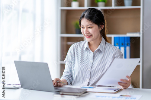 Young woman working on a laptop in the office. Asian businesswoman sitting at her workplace in the office. Beautiful Freelancer Woman working online at her home.