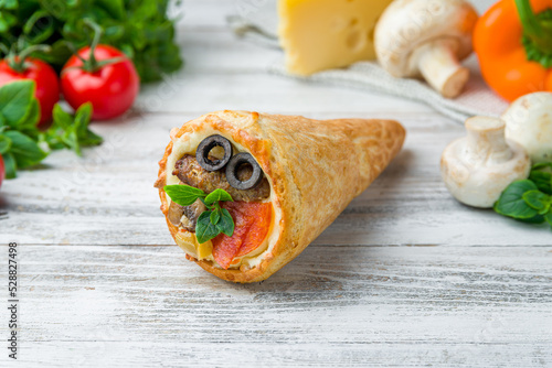 pizza in a cone with meat kebab and pepperoni with black olives and vegetables on white wooden table