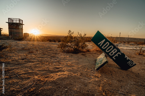 Broken street sign in laying in dirt in the desert with an abandoned tower in the background at sunset