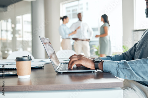 Laptop, work and a business man at a startup working at a desk in an open office with documents. Teamwork, planning and internet research, a manager at a company with a team talking in background.