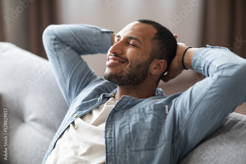 Domestic Comfort. Relaxed Young Black Man Leaning Back On Couch At Home