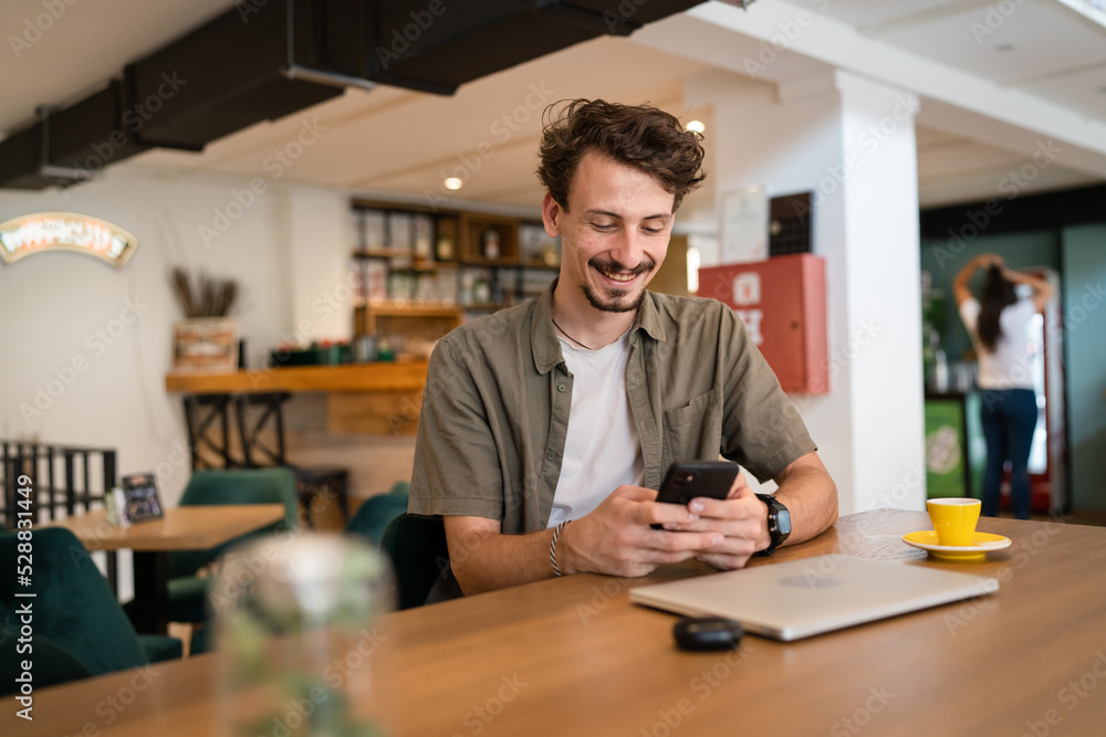 one caucasian man young adult millennial male using mobile phone sit at table in cafe at the table alone happy smile confident having online chat using internet for text messages or social network one caucasian man young adult millennial male using mobile phone sit at table in cafe at the table alone happy smile confident having online chat using internet for text messages or social network