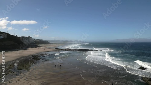 Aerial drone shot at beach with small town in the background during the day.