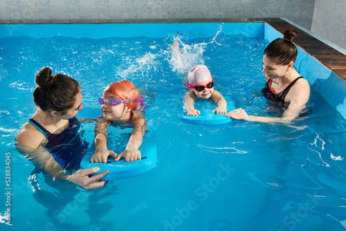 Photo Little girl learning to swim in indoor pool with pool board and trainer