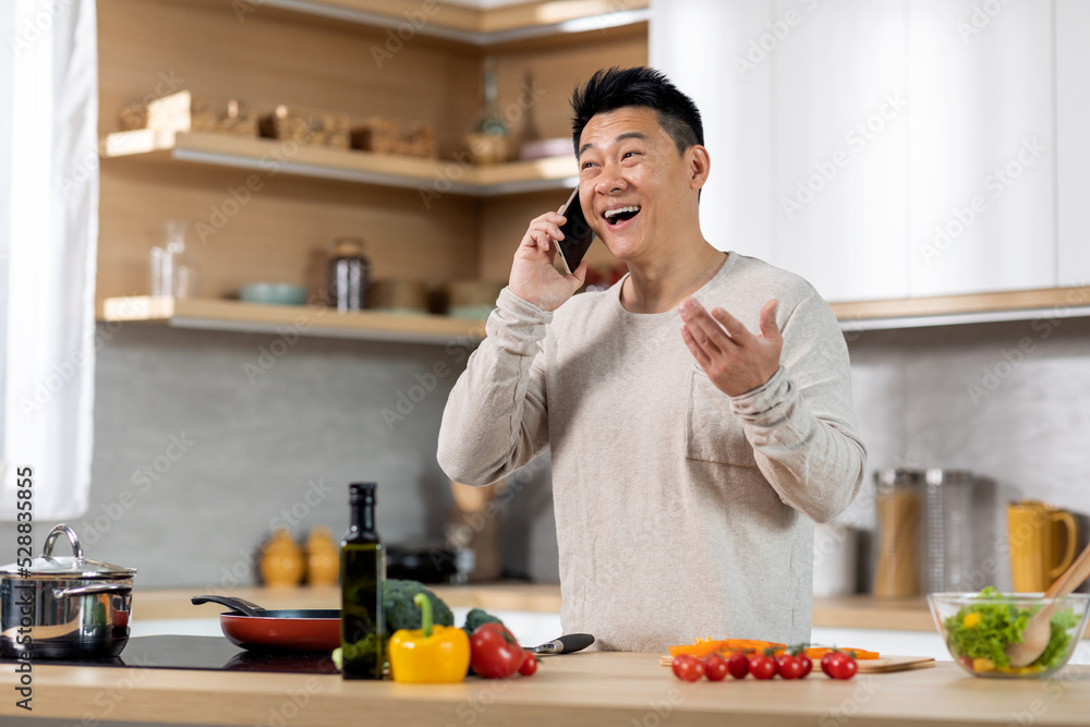 Happy chinese man cooking healthy meal and talking on phone Happy chinese man cooking healthy meal and talking on phone