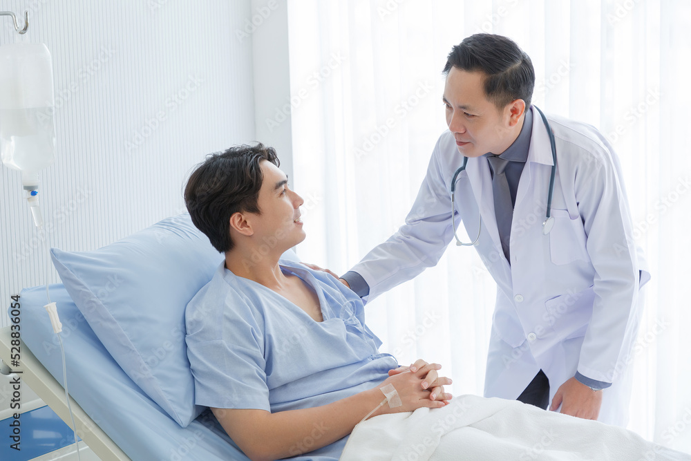 Senior doctor and young male patient who lie on the bed while checking symptom, consult and explain with nurse taking note and supporting in hospital wards. Senior doctor and young male patient who lie on the bed while checking symptom, consult and explain with nurse taking note and supporting in hospital wards.