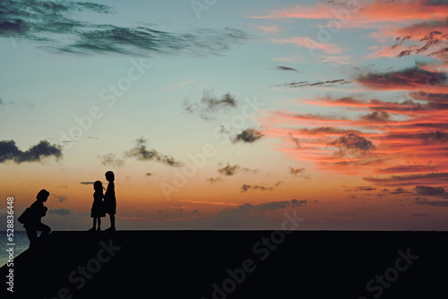 silhouette of children near the ocean at sunset © Ayumu