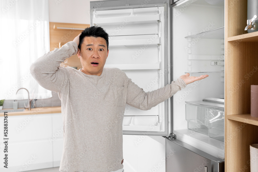 Shocked asian man pointing at empty fridge Shocked asian man pointing at empty fridge