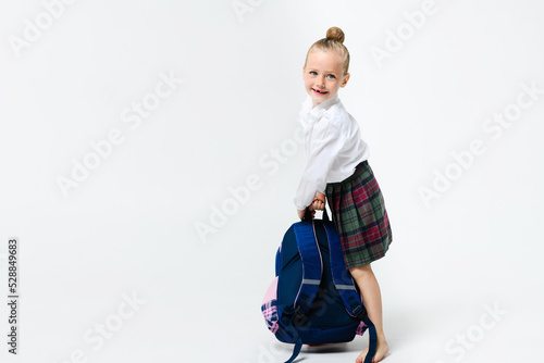 Cute girl in a school uniform with a big backpack on a white background