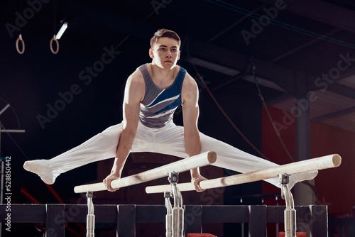 Gym, man and training for balance and fitness in professional gymnastics for cardio sports workout at night. Young athletic guy in dark competitive acrobat exercise in sport practice for competition.