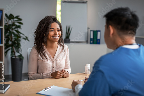 Happy pretty young african american woman patient in consultation with asian man doctor in uniform