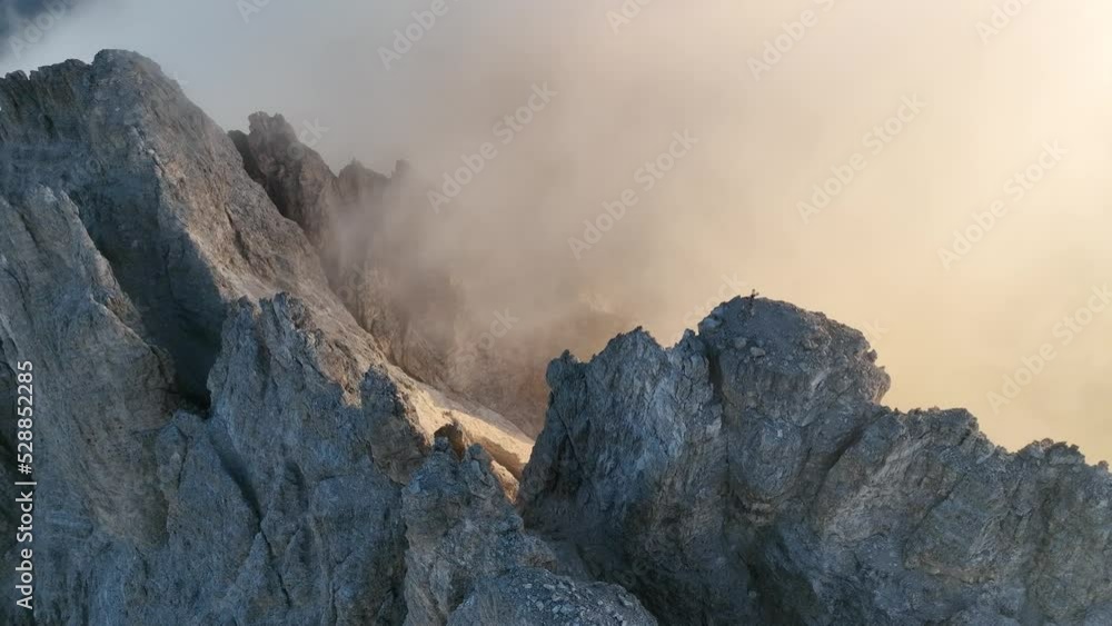 Dynamic shot of a mountain covered partially by fog and the rising sun in the background