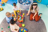 Playtime at nursery school. Toddlers with their teacher sitting on the floor and playing with building blocks, colorful cars and other toys. High quality photo