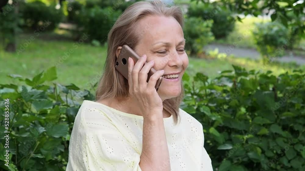 Mature woman talking on mobile phone in the park on a summer day. Mature woman talking on mobile phone in the park on a summer day.