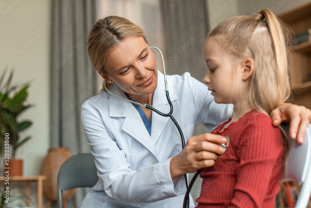 Cheerful female pediatrician holding stethoscope and examining child girl patient, checking heart lungs of kid Cheerful female pediatrician holding stethoscope and examining child girl patient, checking heart lungs of kid