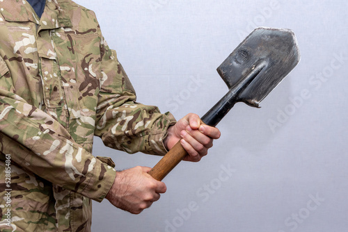 A soldier in an American military uniform holds a sapper shovel in his hands on a light background. photo