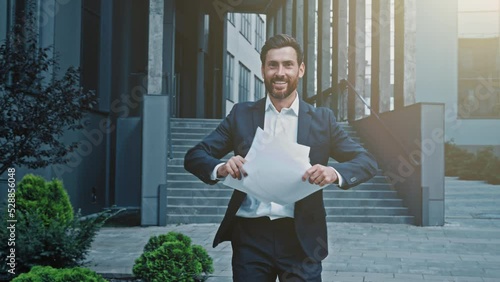 Happy businessman walking outdoors reading report browsing documents reads good news excited motivated satisfied man celebrating victory throwing papers enjoying success rejoices profitable contract