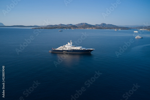 White blue mega yacht anchored off the coast of sardinia aerial view. One of the largest yachts on dark blue water in the background coastline, mountains, blue sky top view. © Berg