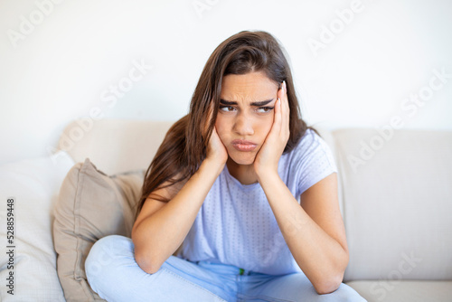 Sad and depressed young woman sitting on a couch in the living room at home