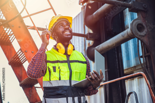 Black African male worker working in port cargo radio control loading container in logistic industry.