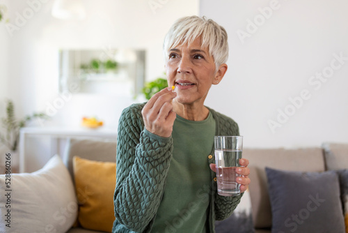 Senior woman takes pill with glass of water in hand. photo