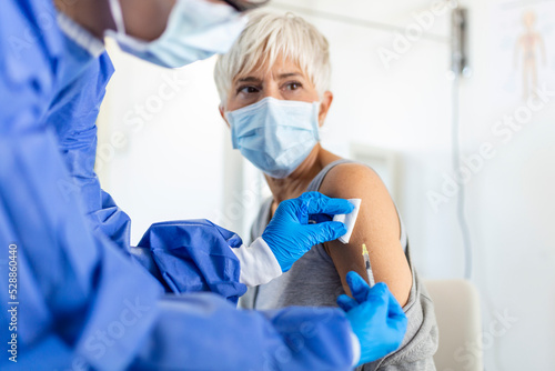 Doctor holding syringe making covid 19 vaccination injection dose in shoulder of female patient wearing mask. Flu influenza vaccine clinical trials concept  corona virus treatment  close up view.