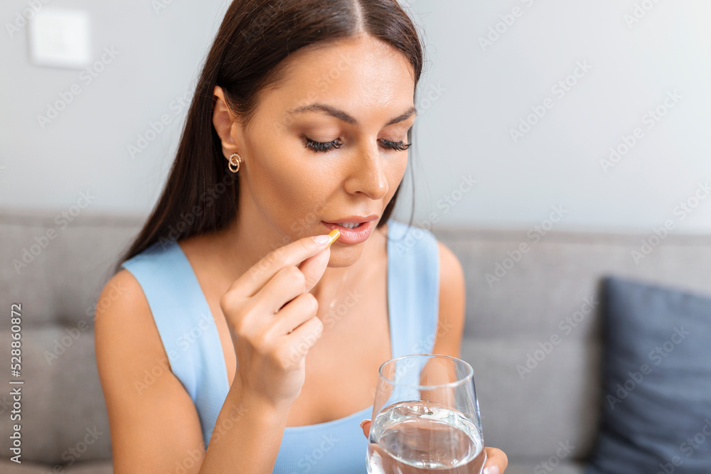 Depressed woman holding pill and glass of water taking painkiller to relieve pain, medicine supplements vitamins, antibiotic medication, meds for old person concept, close up view Depressed woman holding pill and glass of water taking painkiller to relieve pain, medicine supplements vitamins, antibiotic medication, meds for old person concept, close up view