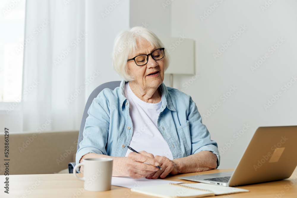 a happy elderly woman is sitting at her desk at home and holding an online conference on a laptop, listening attentively to the information a happy elderly woman is sitting at her desk at home and holding an online conference on a laptop, listening attentively to the information