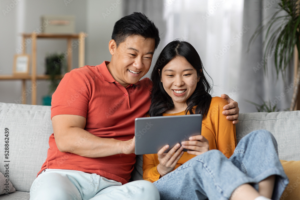 Obraz premium Relaxed japanese family sitting on couch at home, using pad
