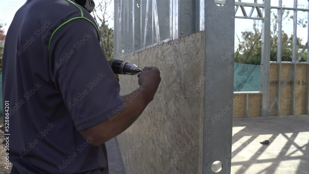 Construction worker screws plywood to metal frame with drill Construction worker screws plywood to metal frame with drill