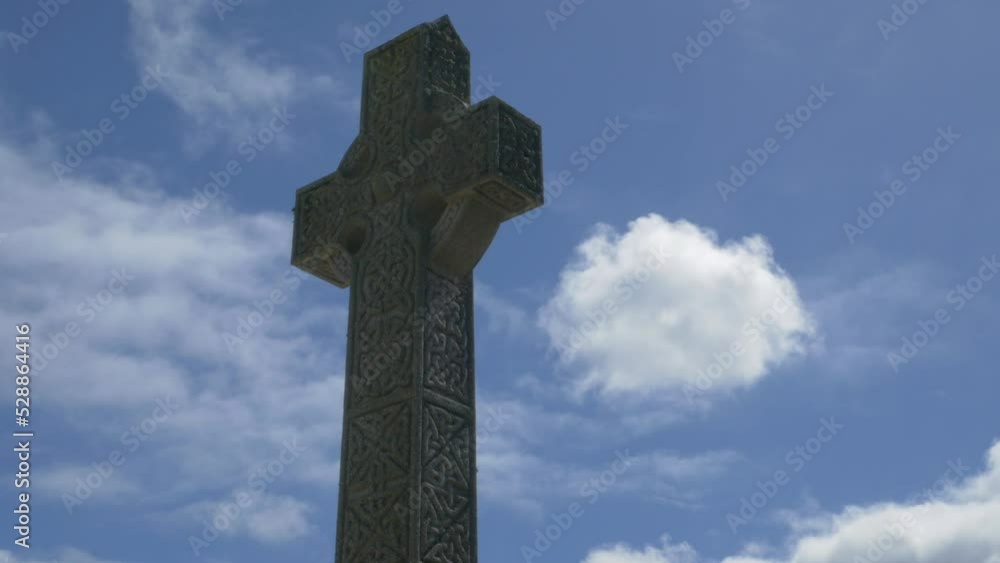 Ornate stone cross against blue sky and clouds Ornate stone cross against blue sky and clouds