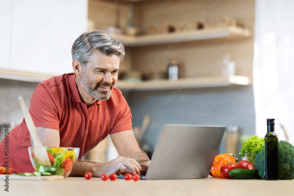 Cheerful grey-haired man cooking at home, reading food blog Cheerful grey-haired man cooking at home, reading food blog