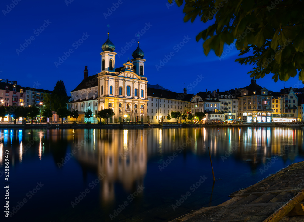 Luzern, Switzerland, July 11, 2022: Night view of the Jesuit Church in Lucerne and its reflection in the Reuss River, Switzerland