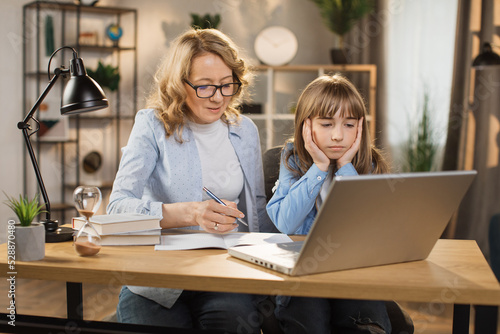 Caucasian tutor engaged with schoolgirl help complete tasks sitting at table at home. Concept of education child development, little child homeschooling writing homework with stepmother.