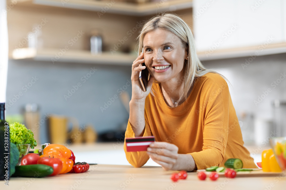 Cheerful blonde lady holding credit card, having phone conversation Cheerful blonde lady holding credit card, having phone conversation