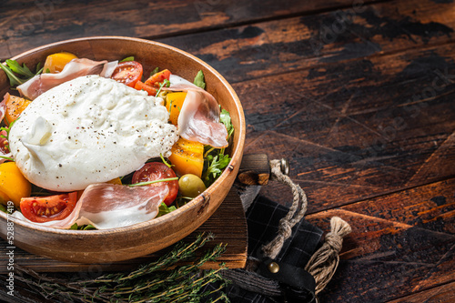 Italian tomatoes and burrata cheese salad with arugula, prosciutto ham and olives. Wooden background. Top view. Copy space