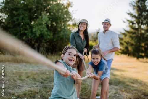 Young family with happy kids having fun together outdoors pulling rope in summer nature.