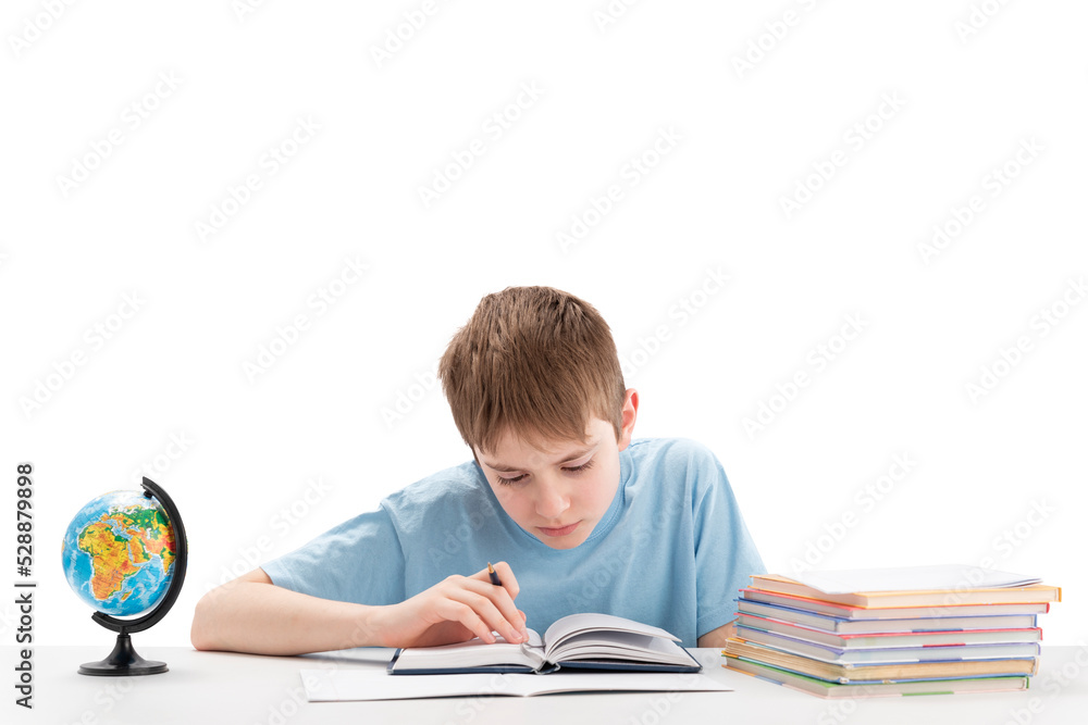 Smiling boy sits at table with stack of notebooks doing homework. Education abroad. International education. White background Smiling boy sits at table with stack of notebooks doing homework. Education abroad. International education. White background