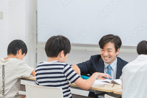 小学生に勉強を教える笑顔の塾講師・先生（日本人男性） 