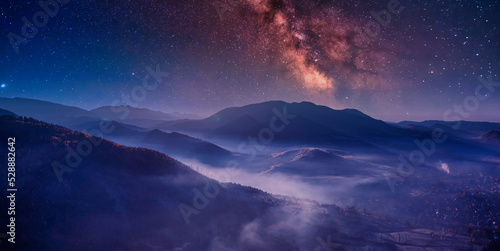 Night in the autumn mountains. Starry sky, yellow leafy trees and fog. photo