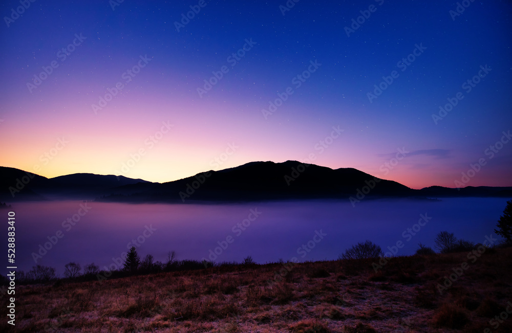 Night in the autumn mountains. Starry sky, yellow leafy trees and fog.
