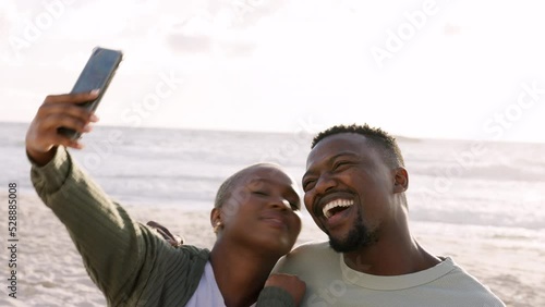 Happy black couple taking selfie at the beach, kiss and bonding on a seaside getaway or trip outdoors. Young African American man and woman enjoying their freedom and relationship on holiday