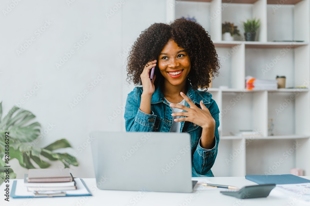 Young female freelancer talking on phone and using laptop at desk. Young female freelancer talking on phone and using laptop at desk.