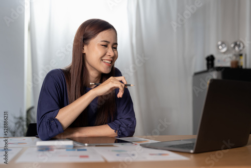 Cheerful woman freelancer working online on laptop, sitting at desk at home, looking at screen.