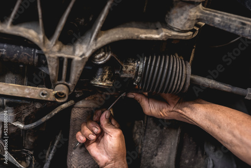 A mechanic inspecting or fixing the steering rack underneath the car at an auto repair shop.