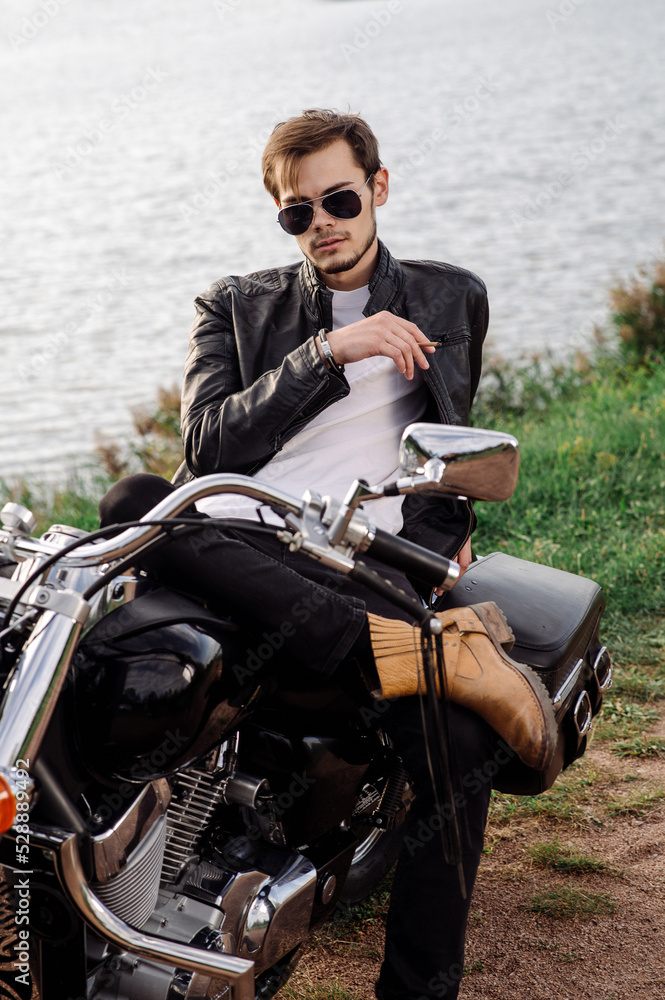 Young handsome male biker is sitting and smoking on motor bike Young handsome male biker is sitting and smoking on motor bike