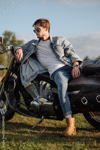 Handsome male biker wearing a jeans clothes is sitting on the motor bike