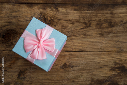 A gift box with pink ribbons placed on a wooden background.
