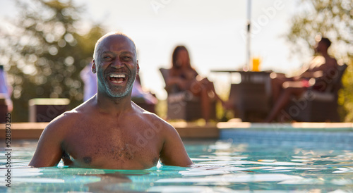 Portrait Of Smiling Senior Man On Summer Holiday Relaxing In Swimming Pool